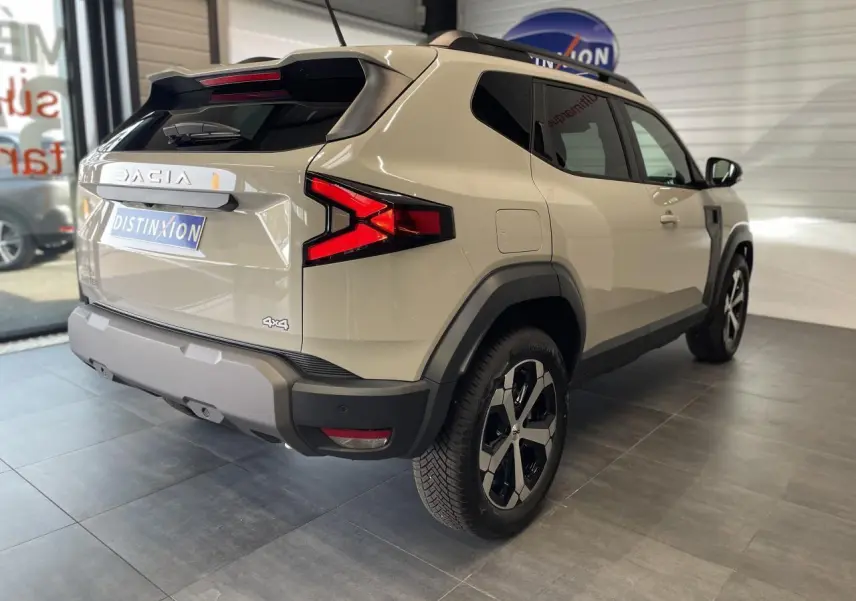 Vue 3/4 arrière droit du SUV Dacia Duster beige avec jantes alliage 18 pouces et barres de toit noires.