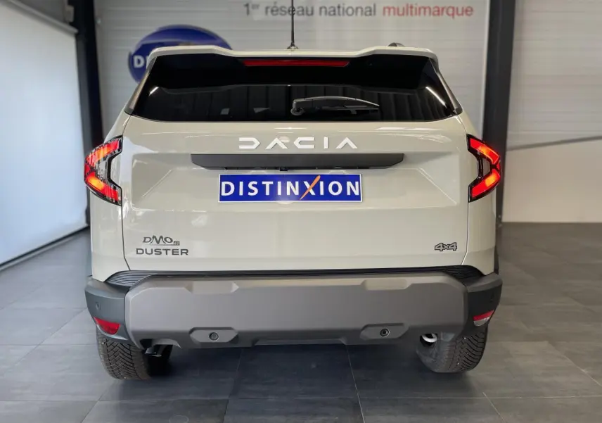 Vue arrière d'un Dacia Duster beige 2025 avec logo DACIA lumineux et badge 4x4 visible sur le hayon.