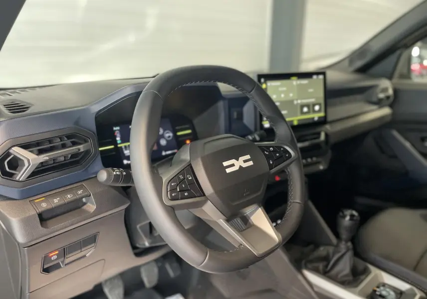 Vue intérieure centrée sur le volant et la console centrale du Dacia Duster 2025 avec boîte manuelle et écran tactile.