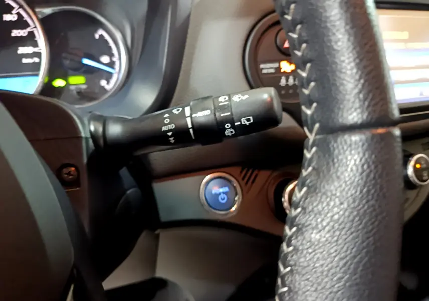 Vue intérieure rapprochée du volant noir et du bouton démarrage bleu de la Toyota Yaris blanche hybride 2020.