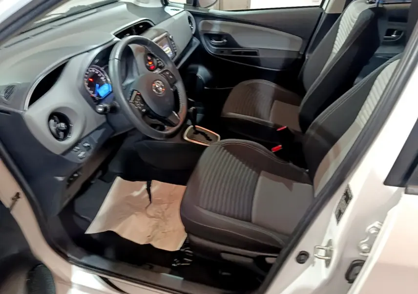 Vue intérieure côté conducteur de la Toyota Yaris blanche 2020, montrant sièges et tableau de bord avec volant multifonction.