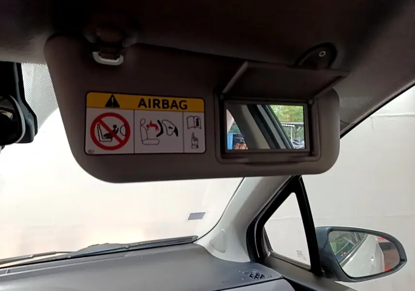 Détail intérieur du pare-soleil côté conducteur de la Toyota Yaris blanche, avec miroir et avertissement airbag visible.