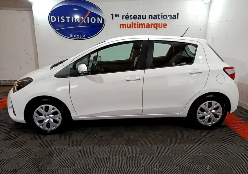 Vue de profil côté gauche d'une Toyota Yaris blanche 2020 hybride, stationnée en intérieur sur sol carrelé.