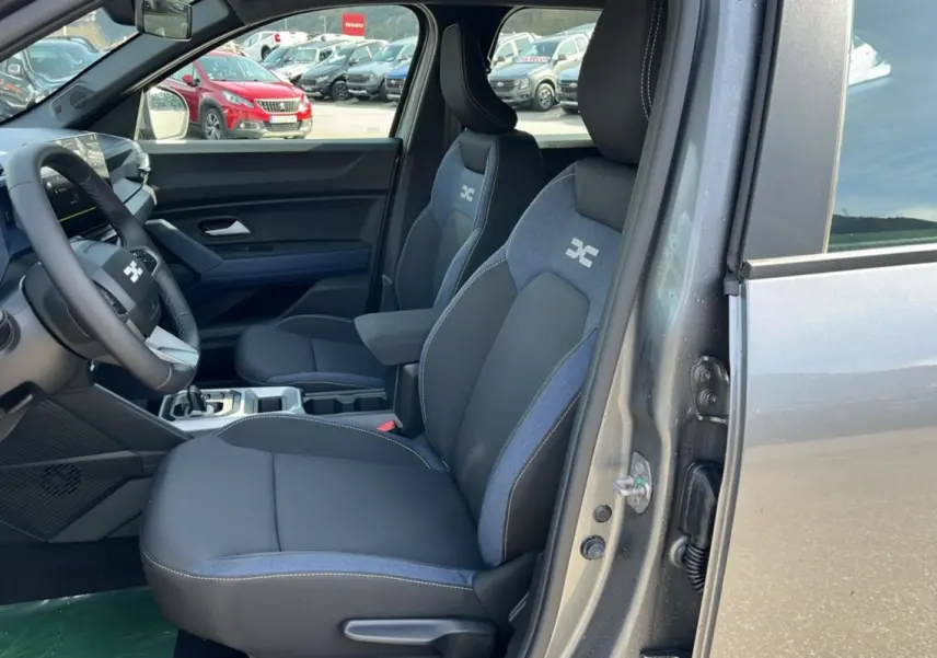 Vue intérieure côté conducteur du Dacia Bigster Hybrid 155 Expression Plus gris schiste, avec sièges tissu bicolore et volant cuir.