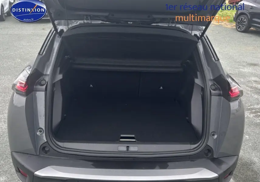 Coffre ouvert vu de l'arrière d'un Peugeot 2008 gris sélénite avec feux arrière LED allumés.