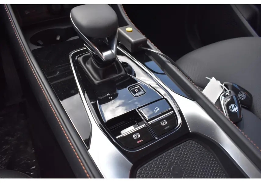 Gros plan sur la console centrale noire brillante du MG Motor EHS gris, avec levier de vitesse automatique et clés sur siège.