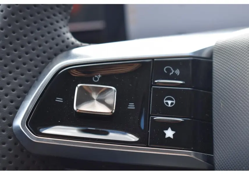 Gros plan sur les commandes multifonctions en plastique noir et chrome du volant perforé du MG MOTOR EHS gris hybride 2026.