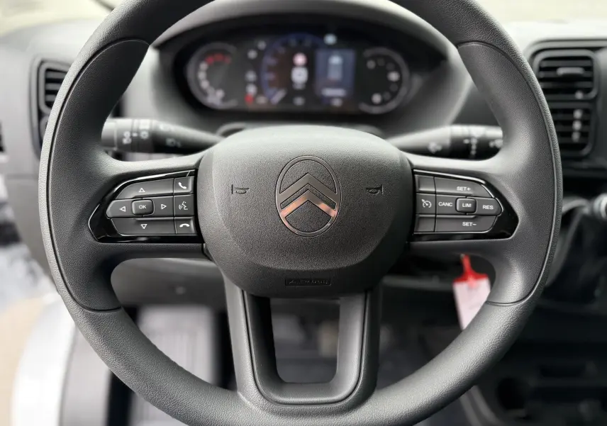 Gros plan sur le volant noir du Citroën Jumper FGN 2025 avec commandes intégrées et tableau de bord flou en arrière-plan.