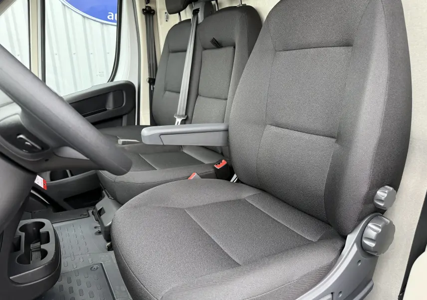 Vue intérieure côté conducteur du Citroën Jumper L3H2 2025, sièges tissu gris foncé et accoudoir central.