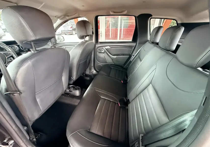 Vue intérieure du Dacia Duster 2017 montrant la banquette arrière en cuir noir et les sièges avant depuis la porte arrière droite ouverte.