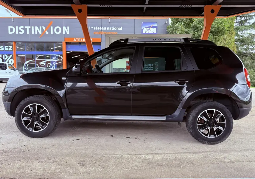 Profil côté gauche d'un Dacia Duster noir métal 2017 avec jantes biton et barres de toit marquées DUSTER.