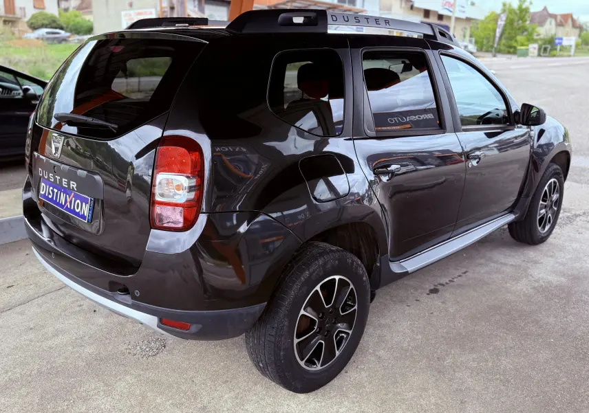 Vue 3/4 arrière droite du Dacia Duster noir métal, avec jantes bi-ton et barres de toit marquées DUSTER.