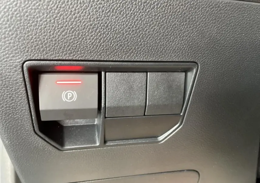 Gros plan sur le bouton de frein de stationnement électrique avec témoin rouge dans l'habitacle du Dacia Duster noir métallisé.