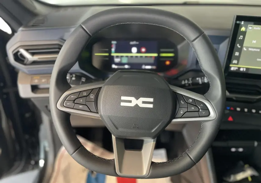 Volant noir du Dacia Duster 2025 avec commandes intégrées, tableau de bord digital et écran tactile central visible.