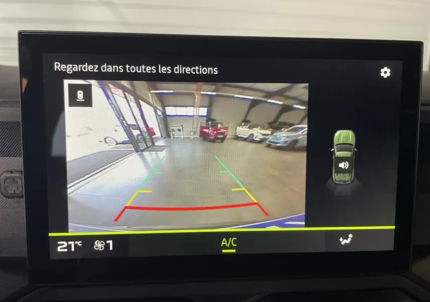 Écran de caméra de recul du Dacia Duster 2025 montrant l'arrière dans un garage avec plusieurs véhicules stationnés.