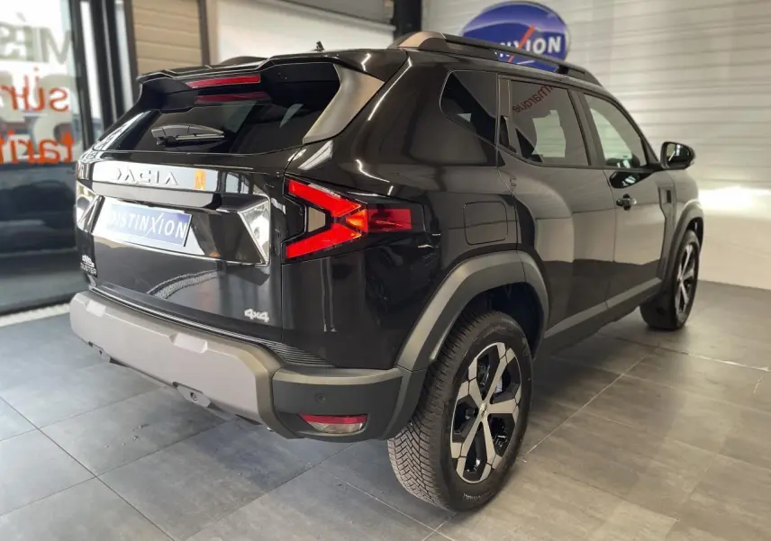 Vue 3/4 arrière droite du SUV Dacia Duster 2025 noir métallisé avec jantes alliage et barres de toit noires.