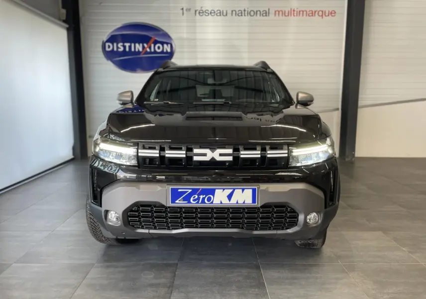 Vue frontale d'un Dacia Duster 2025 noir métallisé avec calandre marquée et plaque Zero KM visible.