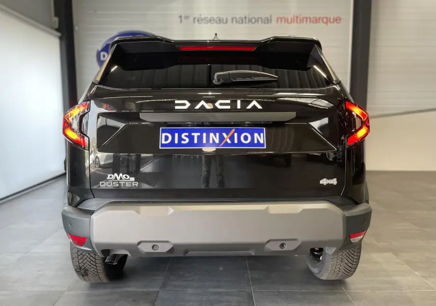 Vue arrière d'un Dacia Duster 2025 noir métallisé avec logo DACIA lumineux et badge 4x4 visible.