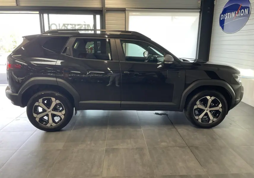 Profil côté gauche du SUV Dacia Duster 2025 noir métallisé avec jantes alliage 18 pouces et barres de toit noires.