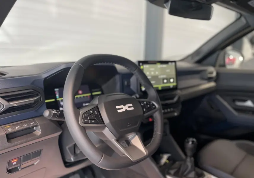 Intérieur du Dacia Duster 2025 vu côté conducteur, volant noir avec logo DC et écran tactile central visible.