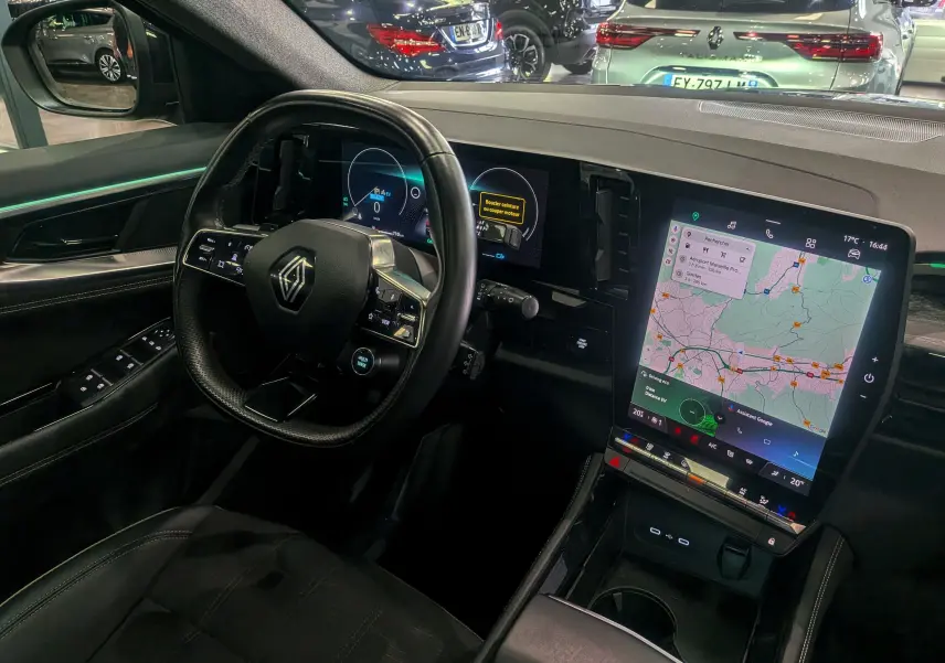 Vue intérieure côté conducteur du Renault Austral E-TECH gris avec tableau de bord numérique et écran tactile central affichant une carte.