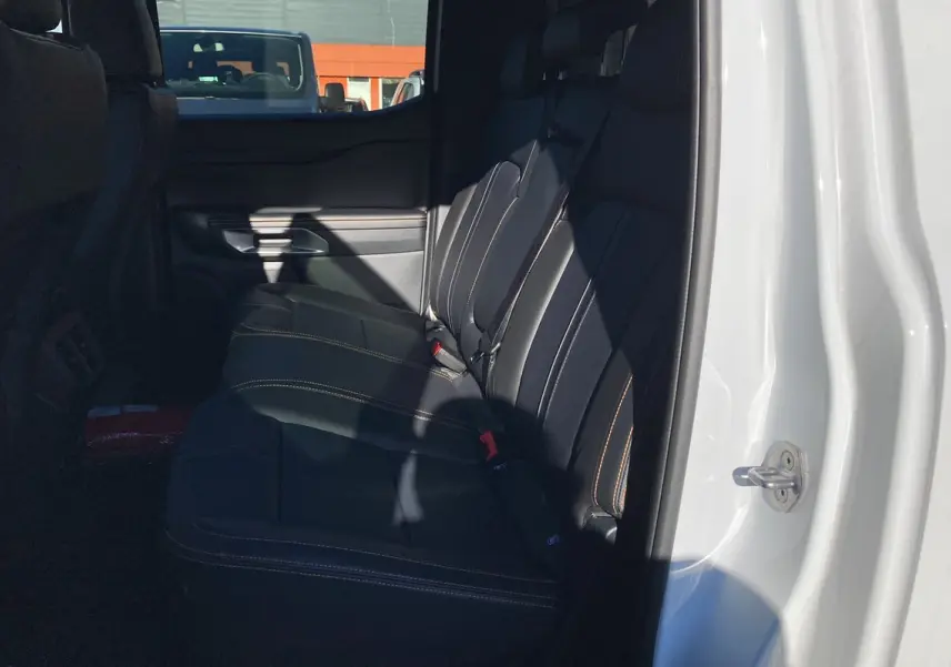 Vue intérieure côté droit sur les sièges arrière en cuir noir avec surpiqûres orange du Ford Ranger blanc glacier 2025 Wildtrak Plus.