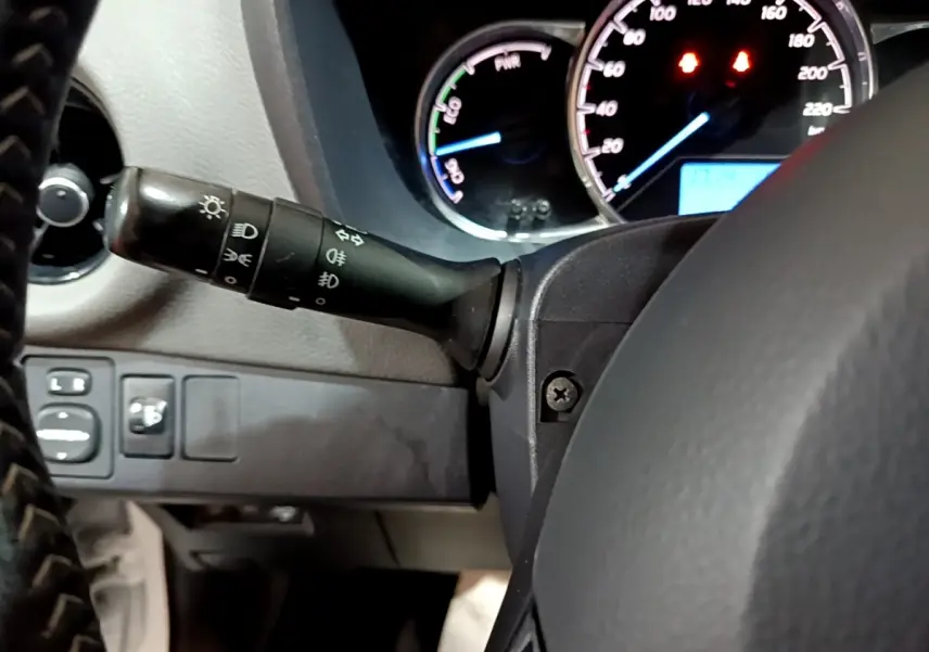 Vue rapprochée du commodo d’éclairage à gauche du volant noir dans l’habitacle d’une Toyota Yaris hybride.