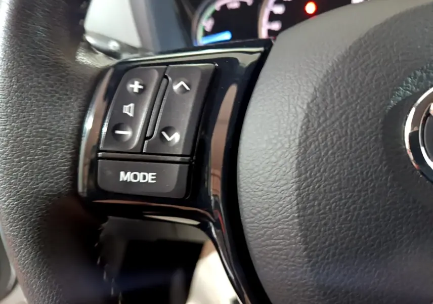 Gros plan sur le volant cuir et alu de la Toyota Yaris blanche, avec commandes multifonctions côté gauche.