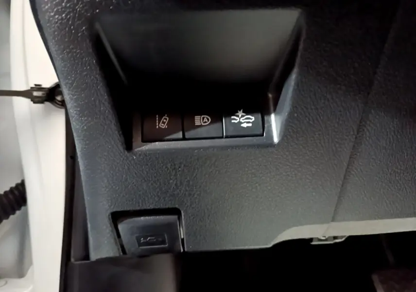 Gros plan sur les commandes de sécurité sous le tableau de bord d'une Toyota Yaris blanche, version hybride.