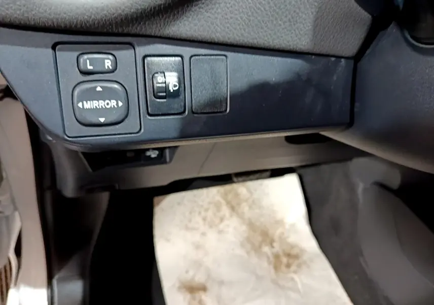 Gros plan sur les commandes de réglage des rétroviseurs côté conducteur dans l’habitacle noir de la Toyota Yaris hybride.