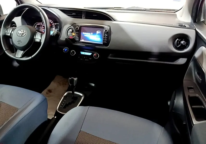 Vue intérieure avant droite de la Toyota Yaris hybride 2019 avec tableau de bord noir et sièges tissu bleu.