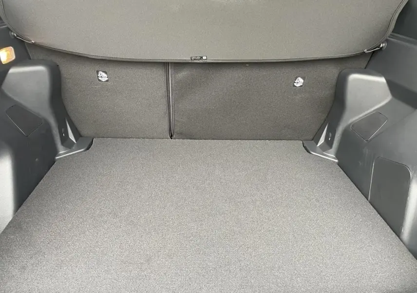 Coffre spacieux de Toyota Yaris Cross 2026 vu de l'intérieur, avec revêtement gris foncé et banquette arrière rabattue.