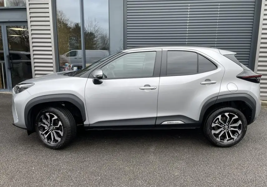 Profil droit d’un Toyota Yaris Cross gris clair 2026 avec jantes alliage noires et logo Yaris Cross sur bas de caisse.