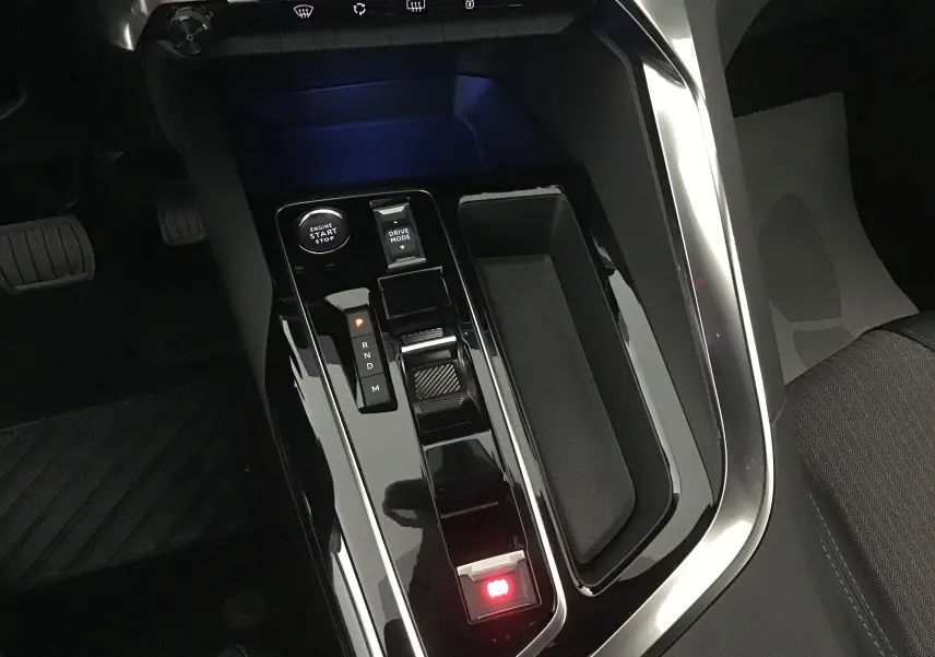 Vue rapprochée de la console centrale noire brillante du Peugeot 5008 2024 avec levier de vitesses automatique et bouton start-stop.