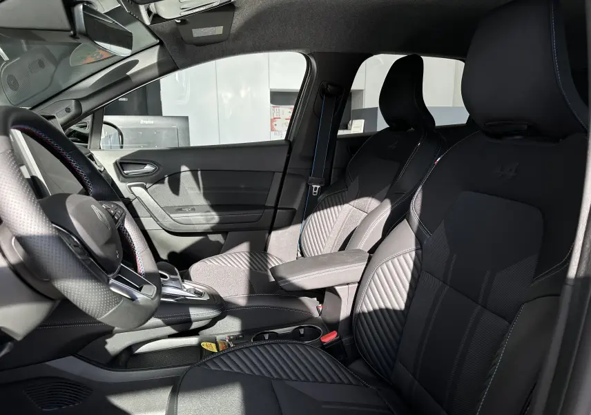 Intérieur avant droit de la Renault SYMBIOZ Esprit Alpine E-Tech 2025, sièges noirs avec logo Alpine et volant cuir tricolore.