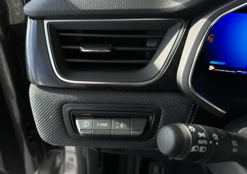 Gros plan sur la console gauche intérieure du Renault Symbioz gris, montrant les commandes E-SAVE et réglage des phares.