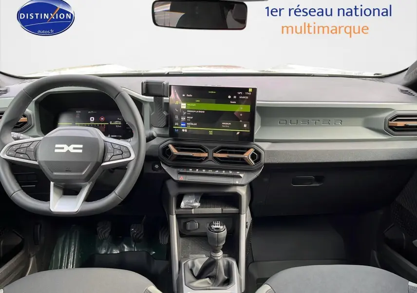 Vue frontale de l'habitacle du Dacia Duster 2025 avec tableau de bord gris et écran tactile central.