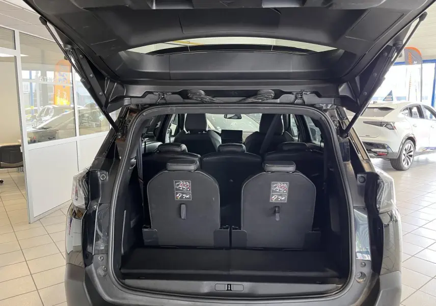Coffre ouvert d'un Peugeot 5008 noir métallisé 2024, montrant les sièges arrière escamotables et l'habitacle intérieur.