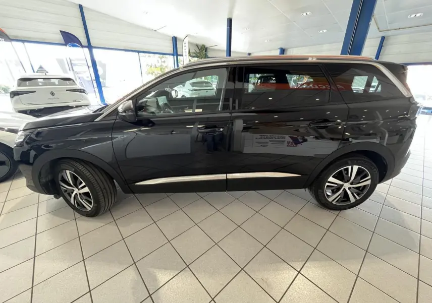 Profil côté gauche du Peugeot 5008 noir métallisé avec jantes alliage bicolores dans un showroom lumineux