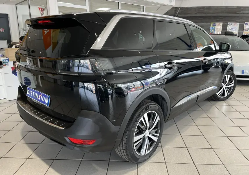 Peugeot 5008 noir métallisé vue 3/4 arrière droit en showroom avec vitres surteintées et jantes alliage bi-ton.