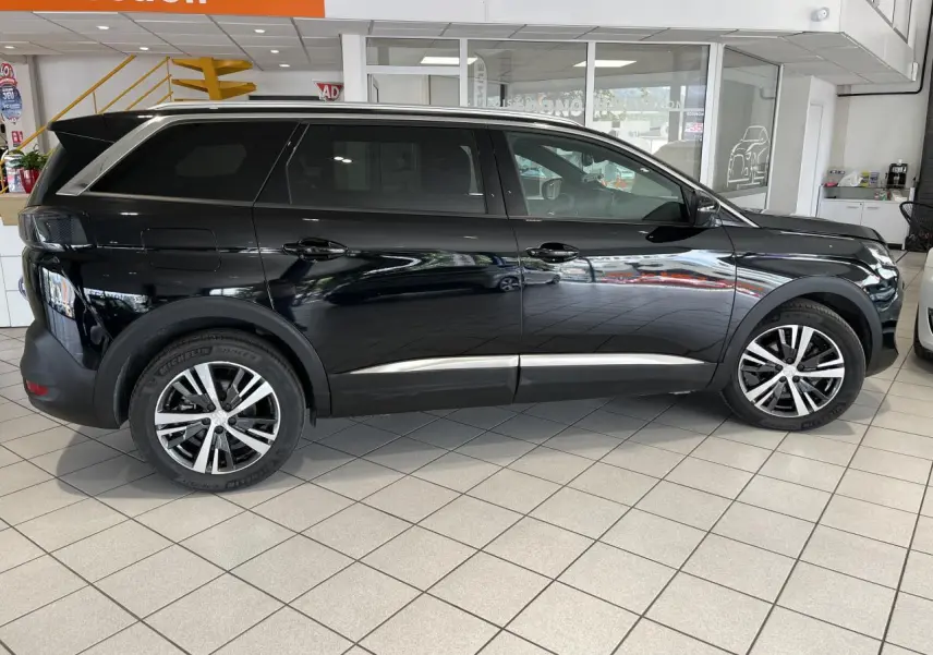 Profil côté gauche d'un Peugeot 5008 noir métallisé 2024 avec jantes alliage bi-ton dans un showroom.