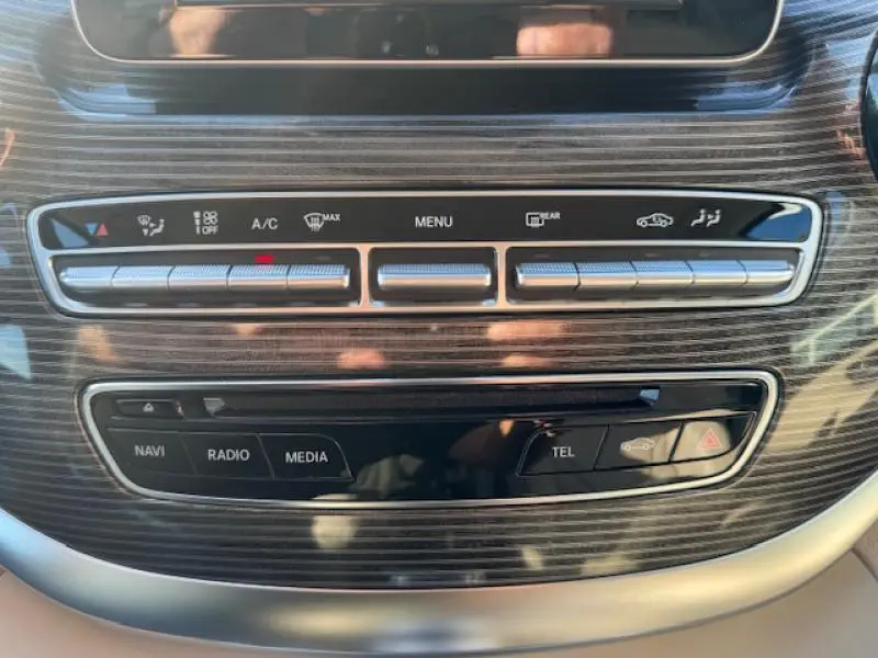 Gros plan sur la console centrale en bois foncé du Mercedes Classe V blanc, avec commandes climatisation et multimédia visibles