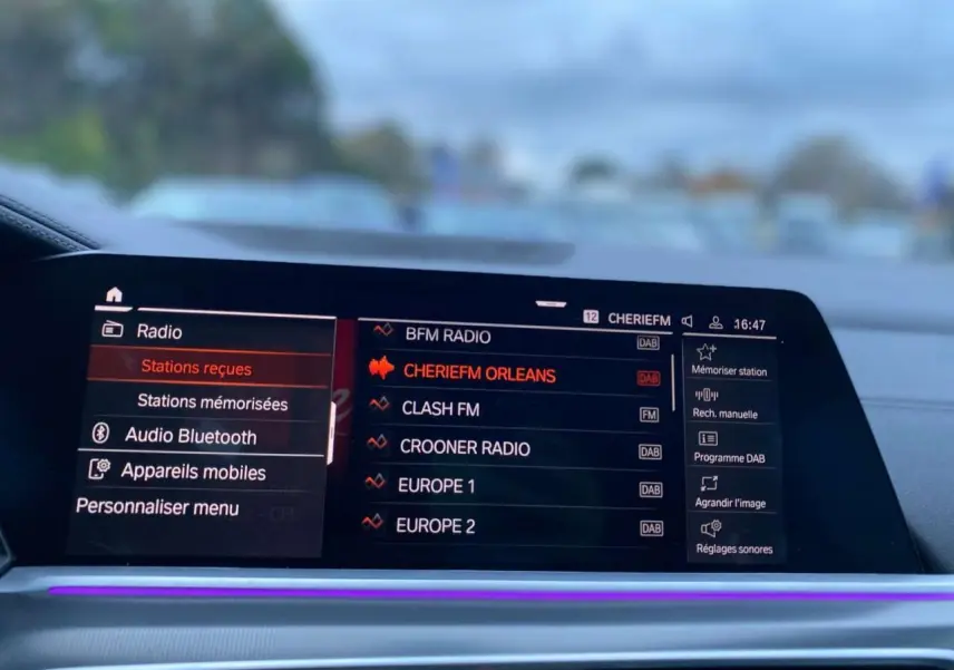 Écran tactile multimédia du BMW X5 blanc 2022, affichant les stations radio avec interface moderne et éclairage d'ambiance violet.