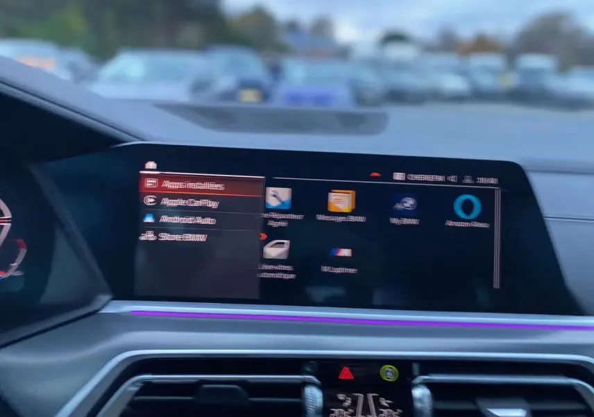 Écran central tactile du tableau de bord du BMW X5 blanc 2022, affichant le menu multimédia avec éclairage d'ambiance violet.
