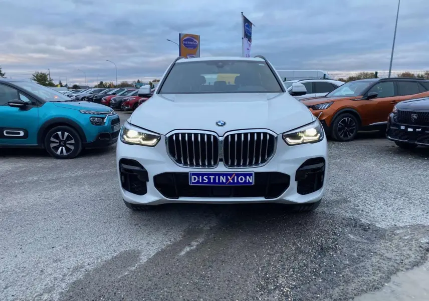BMW X5 xDrive 30d blanc vu de face, phares allumés et calandre imposante en concession extérieure.