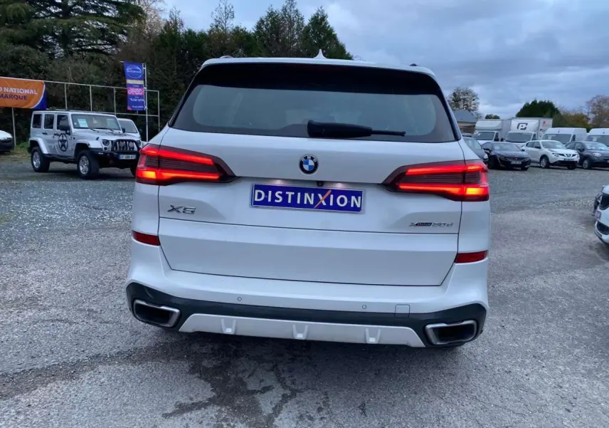 Vue arrière d'un BMW X5 blanc xDrive 30d 2022 avec feux allumés et double sortie d'échappement intégrée au pare-chocs.