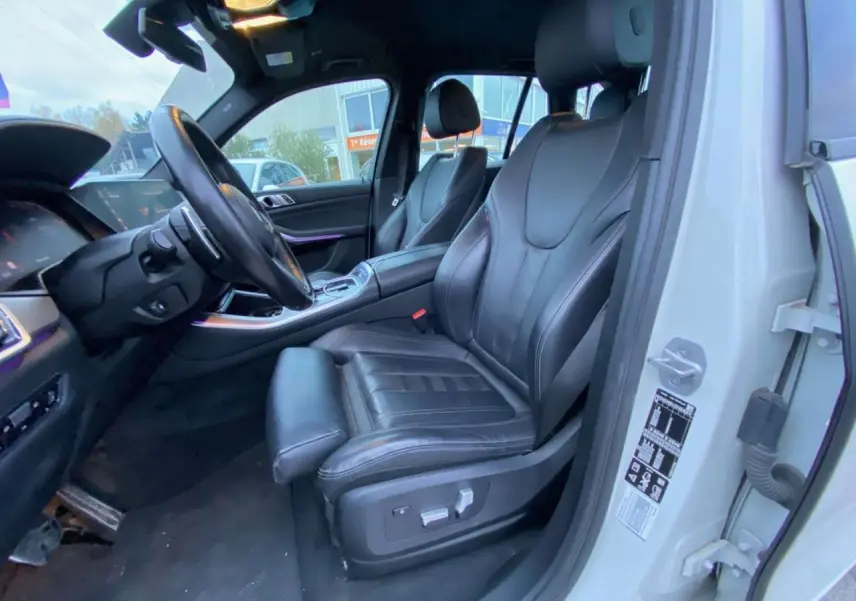 Vue intérieure côté conducteur du BMW X5 blanc 2022, sièges sport en cuir noir et tableau de bord moderne.