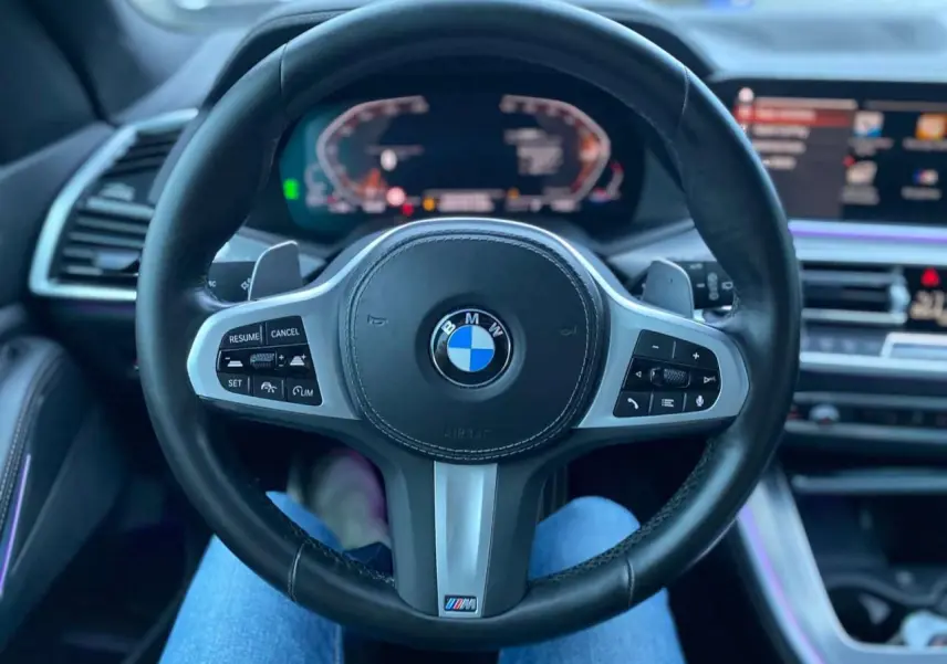 Vue intérieure centrée sur le volant M Sport noir du BMW X5 blanc xDrive 30d 2022 avec tableau de bord numérique.