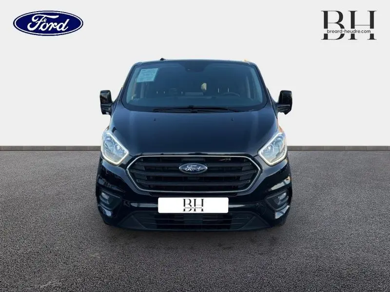 Vue frontale du Ford Transit Custom Fourgon noir Agate métallisé, avec calandre chromée et phares allumés.