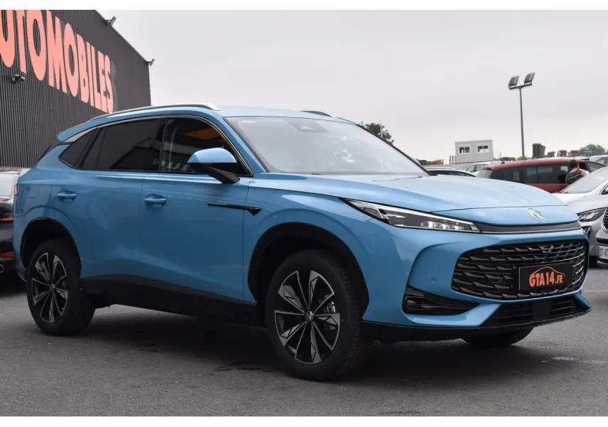 Vue 3/4 avant d'un MG MOTOR EHS bleu 2026 avec jantes alliage noires et phares LED fins, stationné en extérieur.